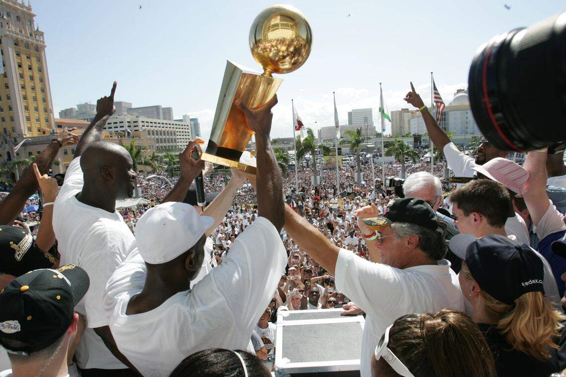 Miami Heat’s Shaquille O’Neal talks to the crowd as Dwyane Wade holds the NBA trophy next to owner Micky Arison on the stage in front of the AAA on June 23, 2006.