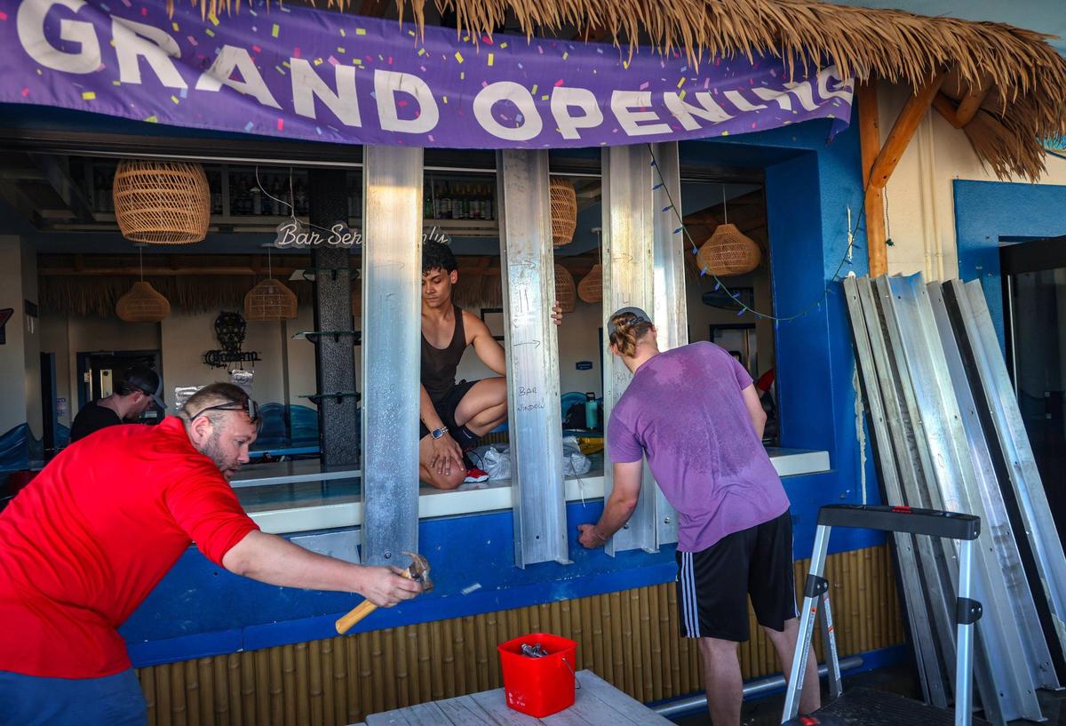 Orlando Vega, 26, center, and Christopher Boyce Jr, 25, right, help Daniel Clarkston, 36, center, in removing metal shutters at Mr. Waves Island, a bar and grill on Fort Myers Beach. Business owners and residents began cleaning up after Hurricane Milton.