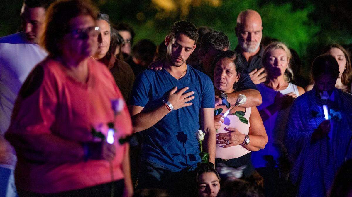 People hold their hands over their hearts during the community beach vigil for those missing and deceased after the partial collapse of Champlain Towers South condominium. They gathered behind the Four Seasons Hotel at The Surf Club in Surfside, Florida, on Monday, June 28, 2021.