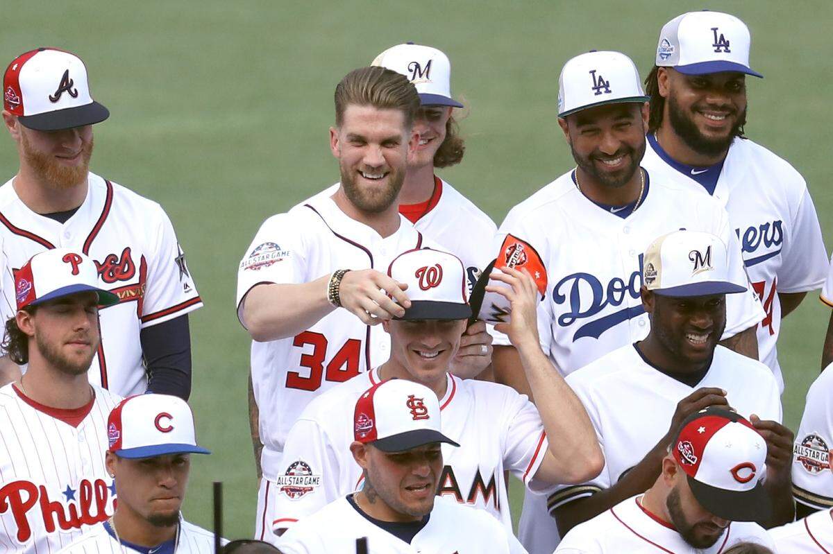 Bryce Harper #34 of the Washington Nationals switches hats with J.T. Realmuto #11 of the Miami Marlins during the National League All-Star team photo during Gatorade All-Star Workout Day at Nationals Park on July 16, 2018 in Washington, DC.