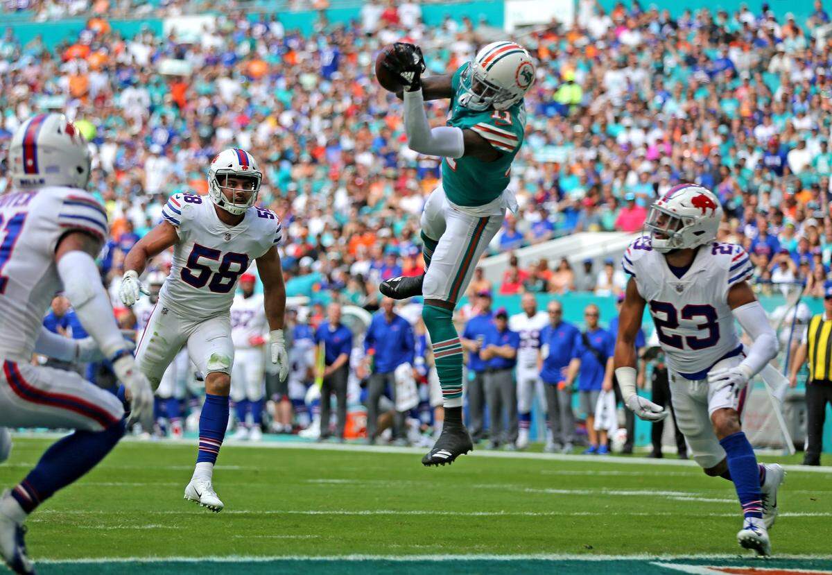Miami Dolphins receiver DeVante Parker (11) catches a first quarter touchdown as Buffalo Bills Matt Milano (58) and Micah Hyde (23) fail to defend at Hard Rock Stadium in Miami Gardens, Florida, Sunday, December, 2, 2018.