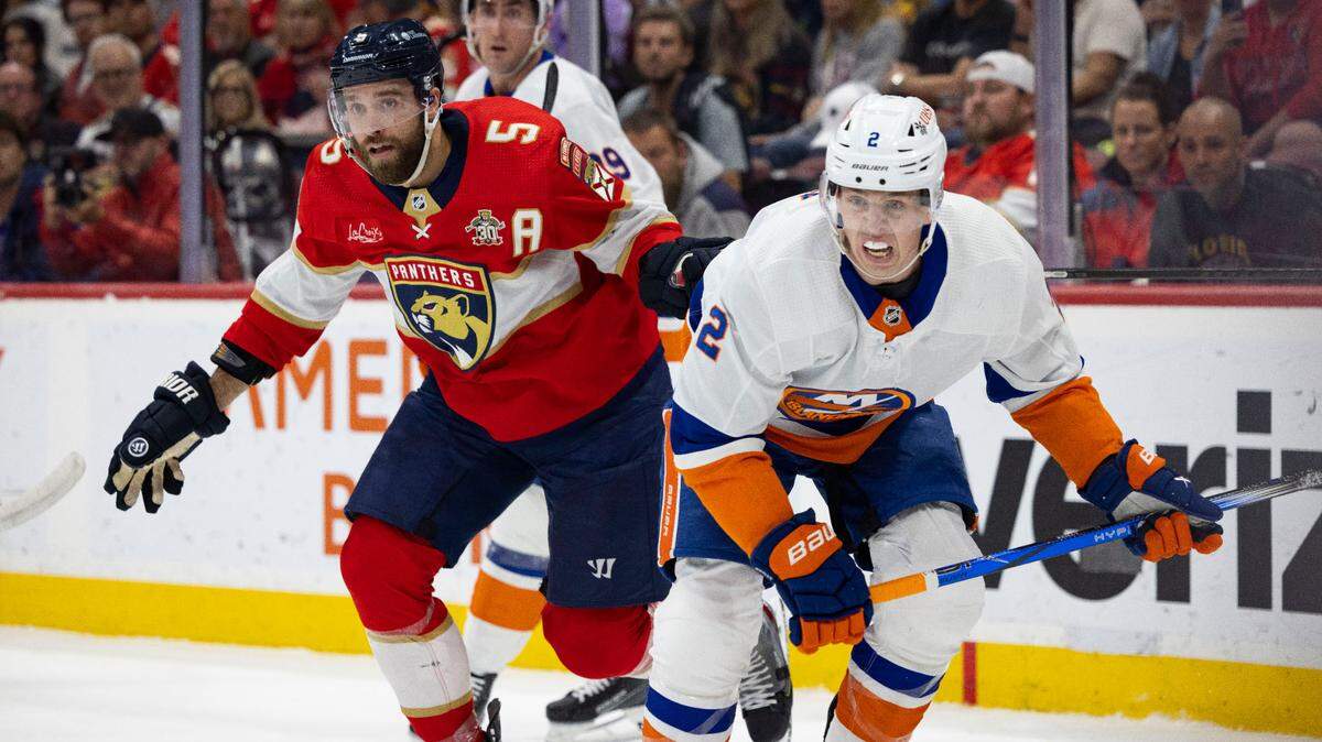 Florida Panthers defenseman Aaron Ekblad (5) and New York Islanders defenseman Mike Reilly (2) look towards the puck during the first period of a game on Thursday, March 28, 2024, at Amerant Bank Arena in Sunrise, Fla.