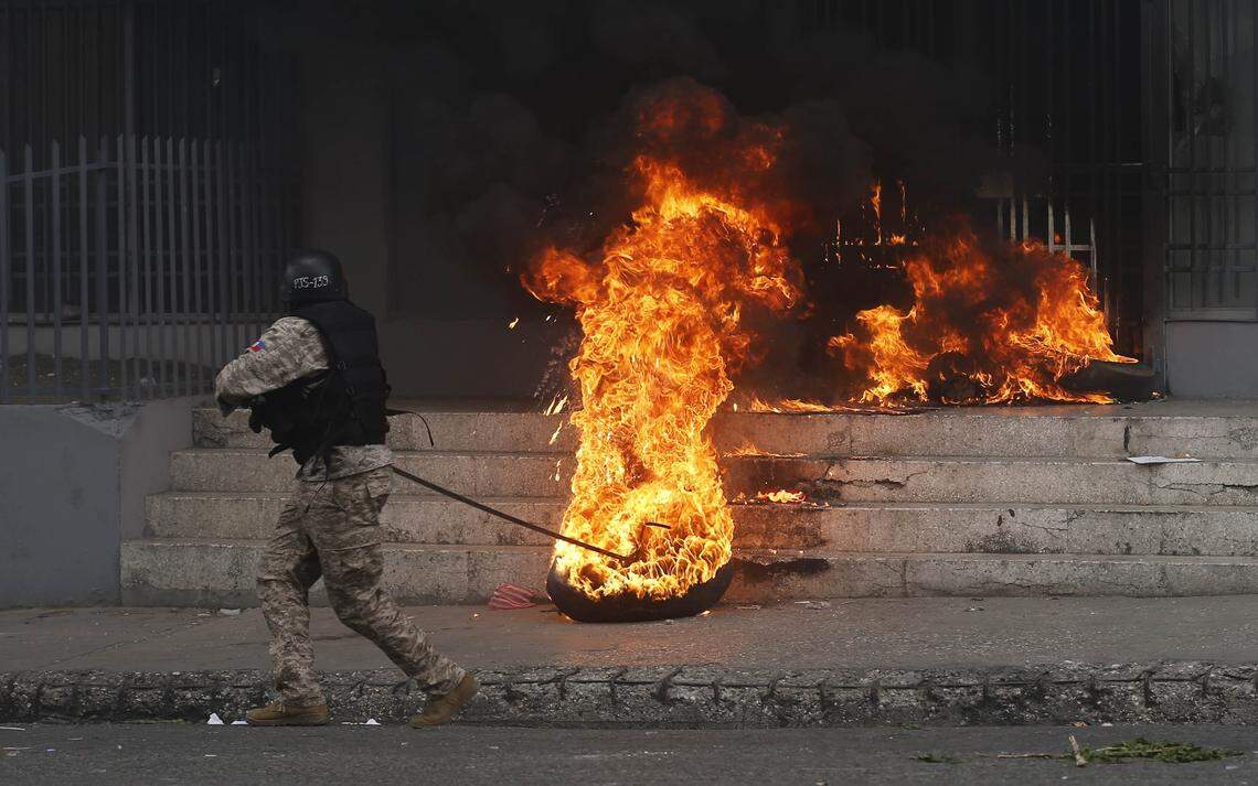 A National police officer removes a burning tire from a government building that was set by anti-government protesters demanding the resignation of President Jovenel Moise in Port-au-Prince, Haiti, Sunday, June 9, 2019. The protesters are demanding further investigation into the fate of funds that resulted from subsidized oil shipments from Venezuela. (AP Photo/Dieu Nalio Chery)
