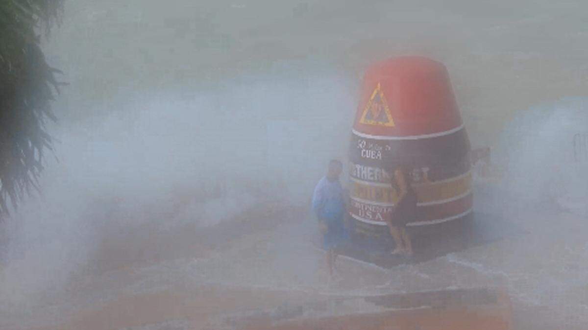 Tourist stand by the Southernmost Point buoy Tuesday morning as waves from Hurricane Idalia splash over the seawall.