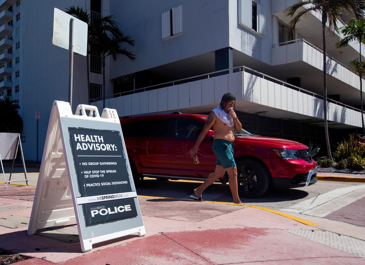 A beach goer covers his mouth as he passes by a health advisory setup by Miami Poloice Department, in response to the coronavirus in Miami Beach, Florida on Sunday, March 15, 2020.