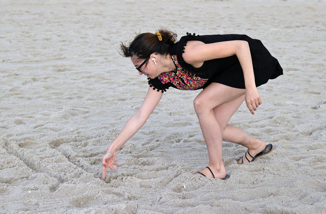 Fayzah Bushnaq, 27, from Virgina writes a message on the sand close to the Champlain Towers South Condo in Surfside, Florida, Friday, June 25, 2021. The apartment building partially collapsed on Thursday, June 24.