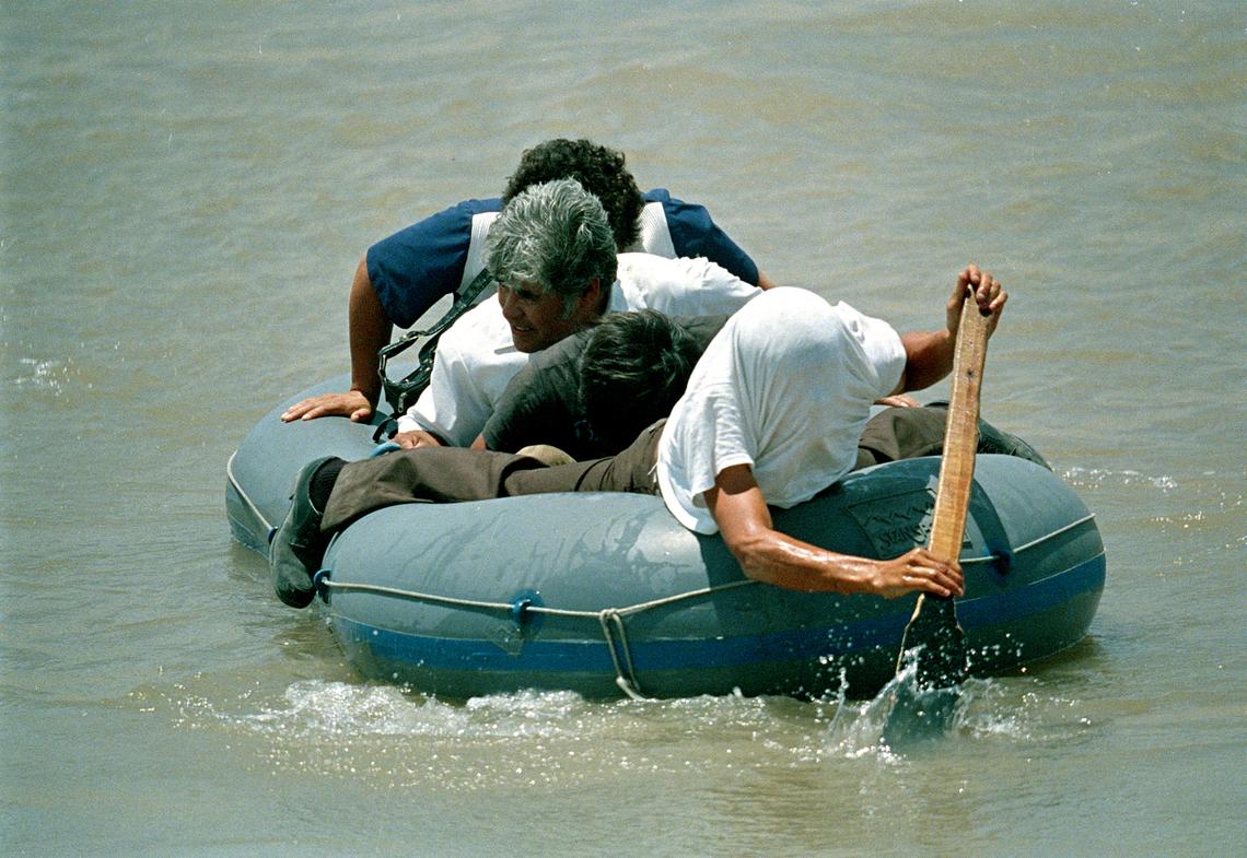A Mexican man hides his face from the camera as he rows his raft with three migrants across the Rio Grande into the United States, at El Paso, Texas, on July 5, 1987. The man made it his business to transport people across the river on rafts.