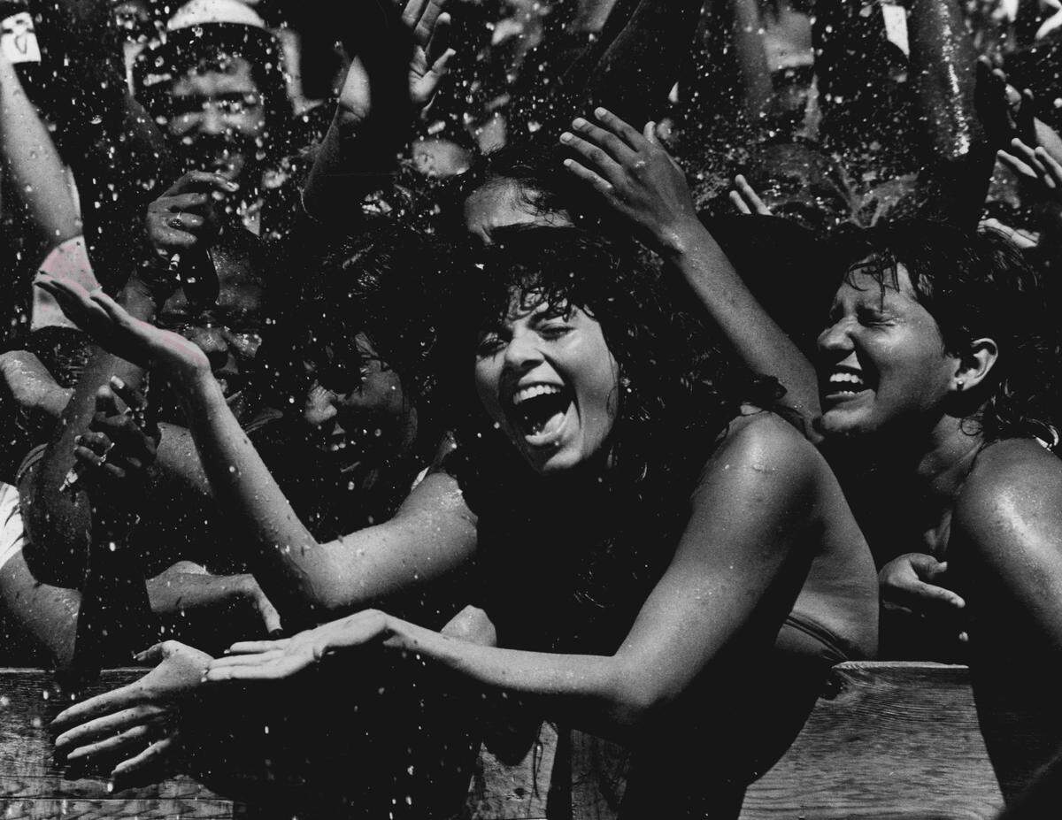 Olga Fernandez, with outstretched arms, and friend Virginia Rodriguez, right, celebrate at a Y-100 event in theearly 1980s. Due to the record- breaking temperatures, WHYI employees doused the crowd in Miami Beach. Musical groups in attendance included: Frank Stallone, the Jonzun Crew, Stacy Lattisaw, Champaign and Al Yankovich.