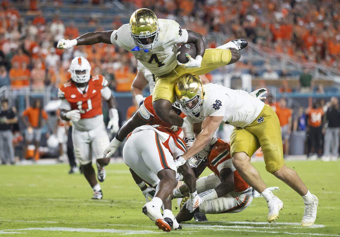 Notre Dame Fighting Irish running back Jeremiyah Love (4) jumps with the ball as Miami Hurricanes defensive back Keionte Scott (0) defends in the second half of their NCAA football game at Hard Rock Stadium on Sunday, Aug. 31, 2025, in Miami Gardens, Fla.
