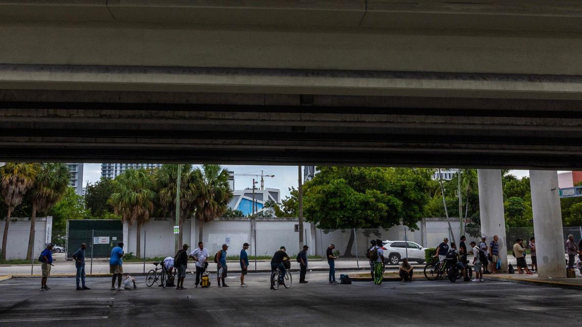 People experiencing homelessness stand in line underneath the expressway while waiting for the nonprofit One World One Heart to deliver free meals on Thursday, Sept. 12, 2024, in Miami.