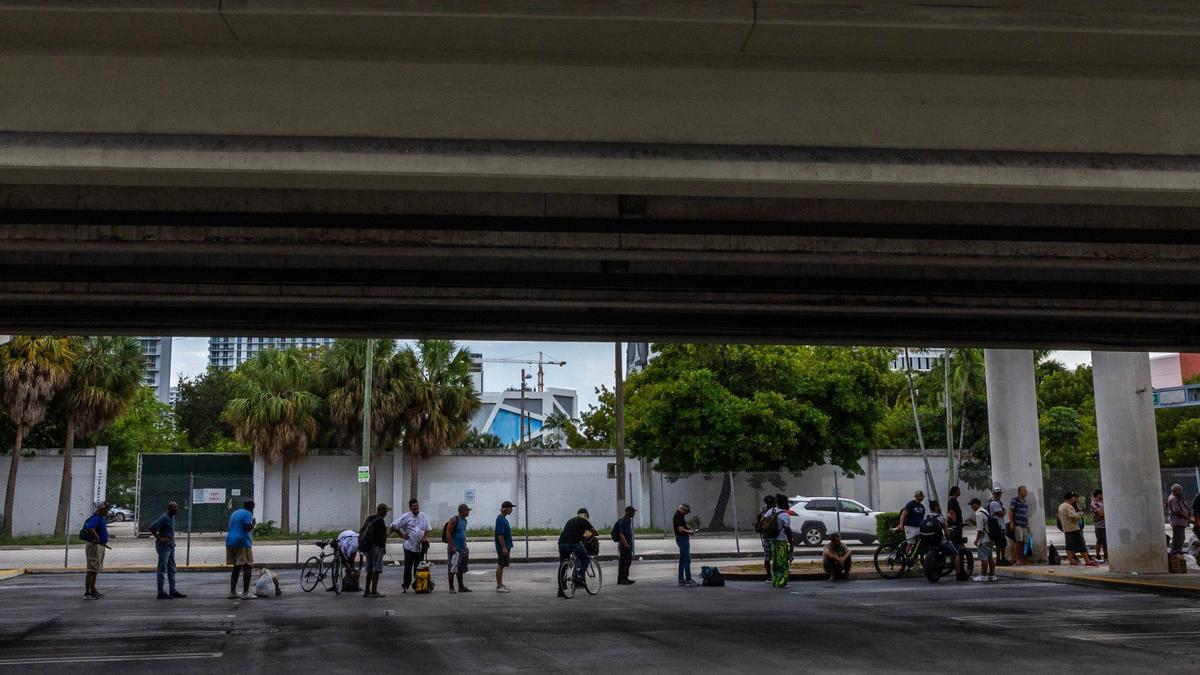 People stand in line underneath the expressway while waiting for the nonprofit One World One Heart to hand out free meals to the homeless population on Thursday, Sept. 12, 2024, in Miami.