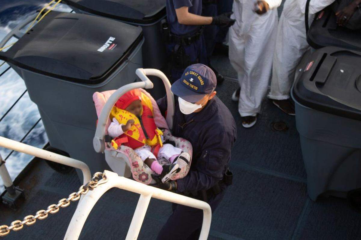 A Coast Guard Cutter Thetis crew member brings a Haitian infant up the stairs of the ship, April 7, 2022. The infant and parent were repatriated to Haiti on April 10, 2022.