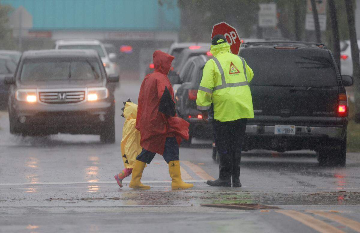 A school crossing guard helps people cross the street in the pouring rain at Dania Elementary School on Wednesday April 12, 2023. Broward public schools will be closed Thursday due to flooding.