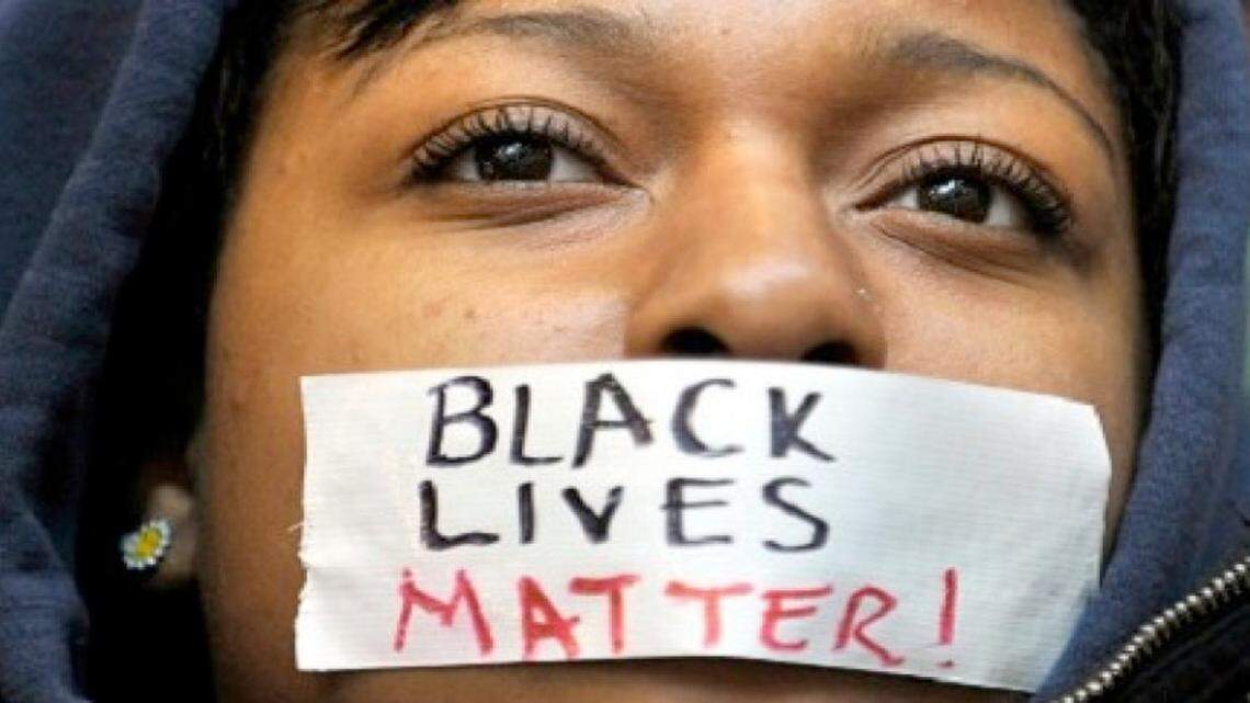 A girl puts a sticker representing the national Black Lives Matter campaign over her mouth.