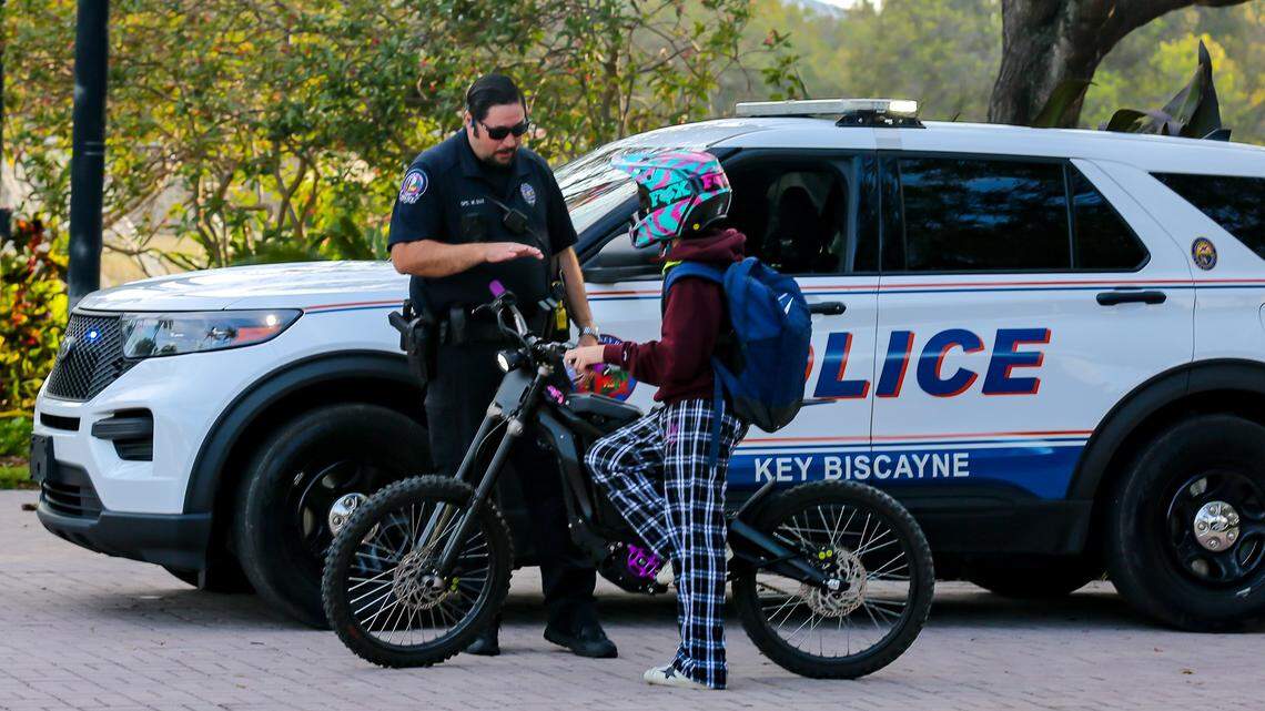 Key Biscayne Officer Marcos Diaz speaks with a boy walking an e-bike, Feb. 17, 2024, a day after a ban on the vehicles  went into effect.