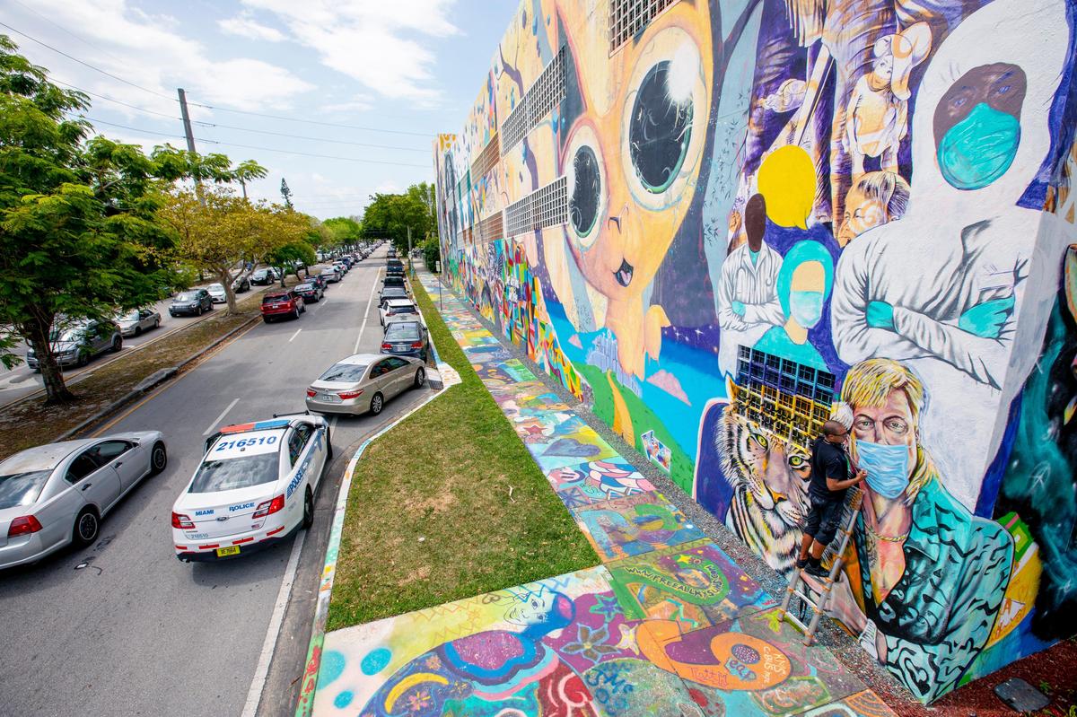 Muralist Kyle Holbrook stands on a ladder as he works to finish the additions to his mural of convict Joe Exotic and a tiger, from the now ubiquitous Netflix docu-series called Tiger King, at 500 NW 36th St as traffic piles up from a Farm Shares food drive nearby, on Tuesday, April 21, 2020.