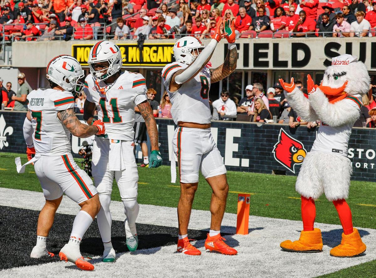 Miami Hurricanes wide receiver Samuel Brown (11) celebrates his touchdown with teammate wide receiver Xavier Restrepo (7) and tight end Elijah Arroyo (8) as Ibis joins them in the end zone during the game against the Louisville Cardinals in the first half during an NCAA football game at L&N Federal Credit Union Stadium in Louisville, Kentucky on Saturday, October 19, 2024.