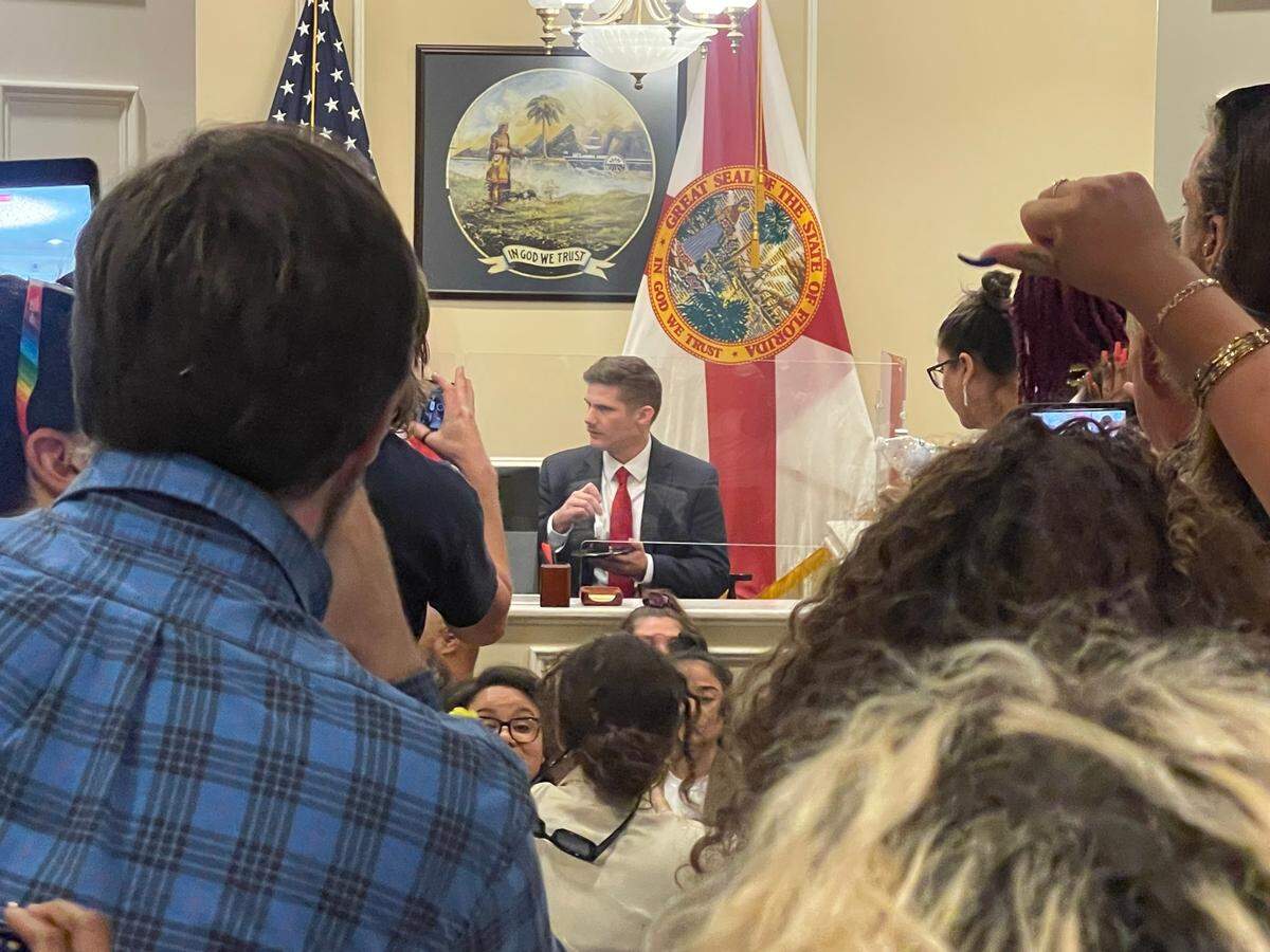Un empleado de la oficina del gobernador Ron DeSantis comiendo pastel de chocolate mientras unas cuantas docenas de manifestantes organizaban una manifestación en la oficina del gobernador en el edificio del Capitolio, en Tallahassee, el miércoles 3 de mayo de 2023.