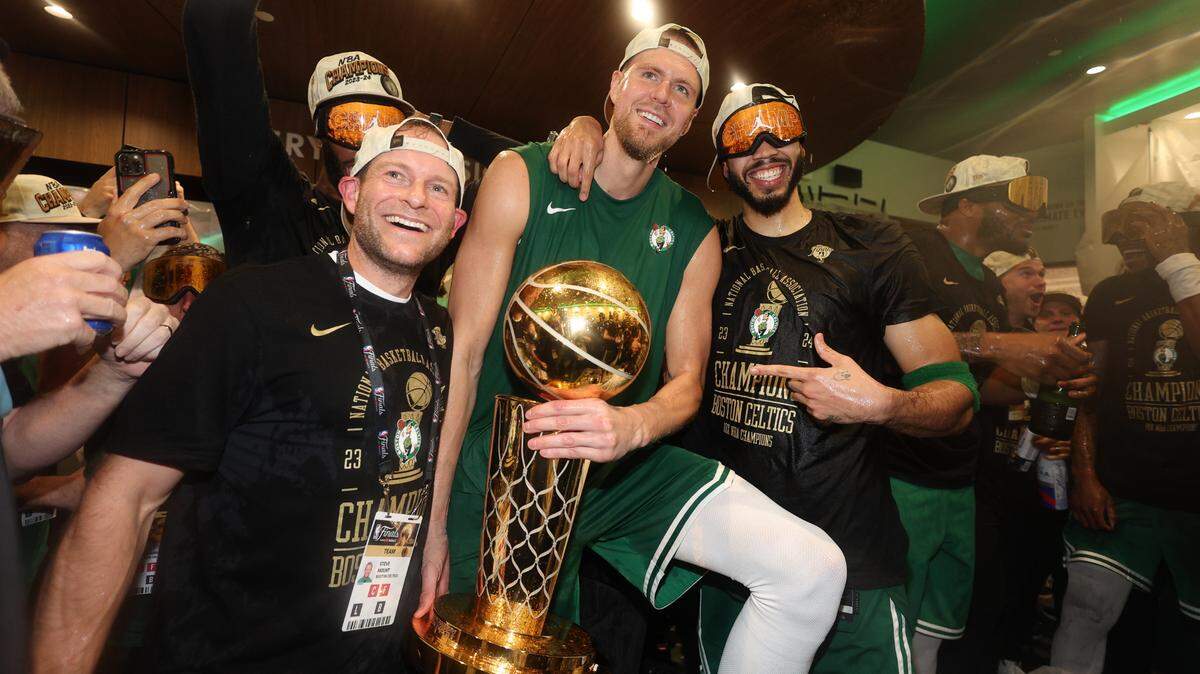 Boston Celtics center Kristaps Porzingis (center) and forward Jayson Tatum (right) celebrate with Celtics director of rehabilitation Steve Mount in the locker room after winning the 2024 NBA Finals against the Dallas Mavericks at TD Garden.