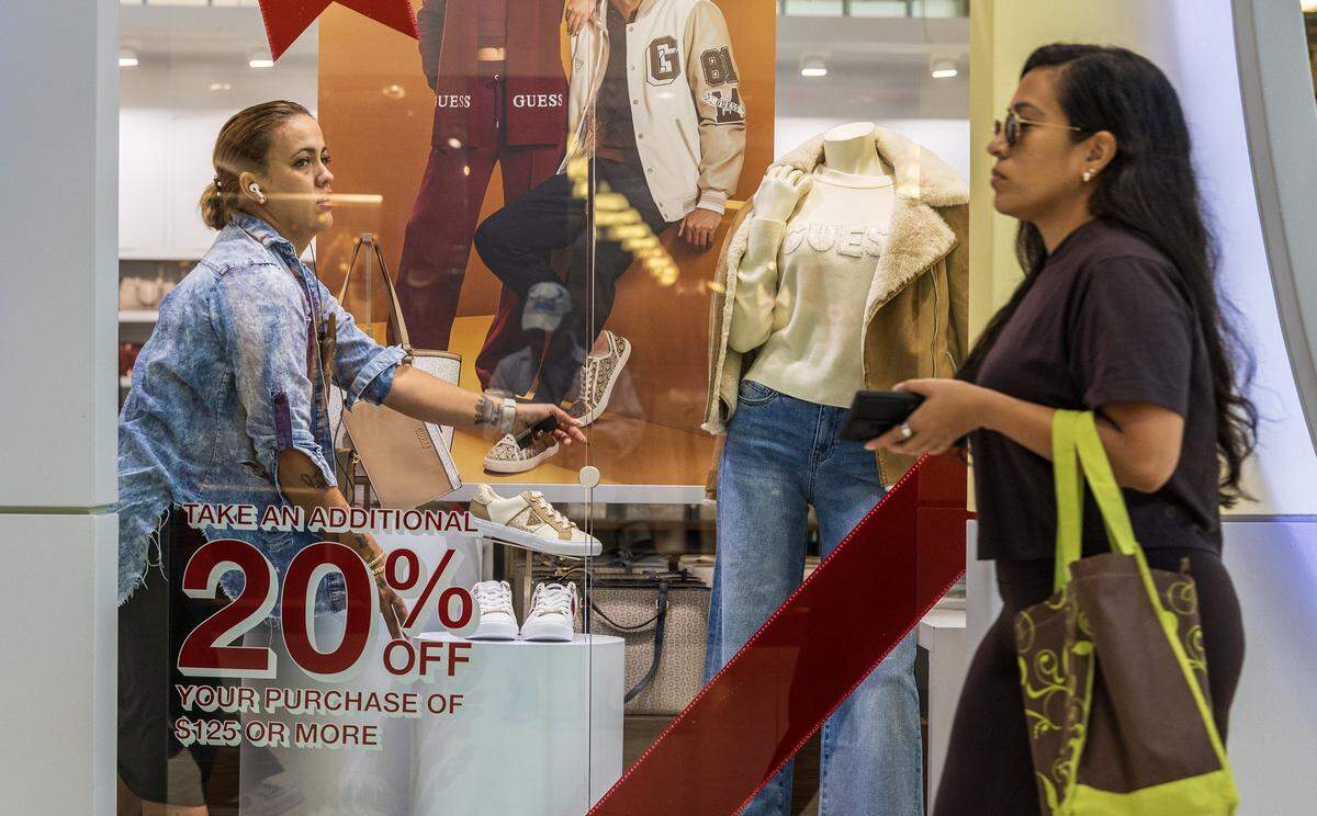 Orquidea Duarte, an assistant manager at the Guess store, sets up promotions banners at the Dolphin Mall on Friday, Nov. 21, 2025.