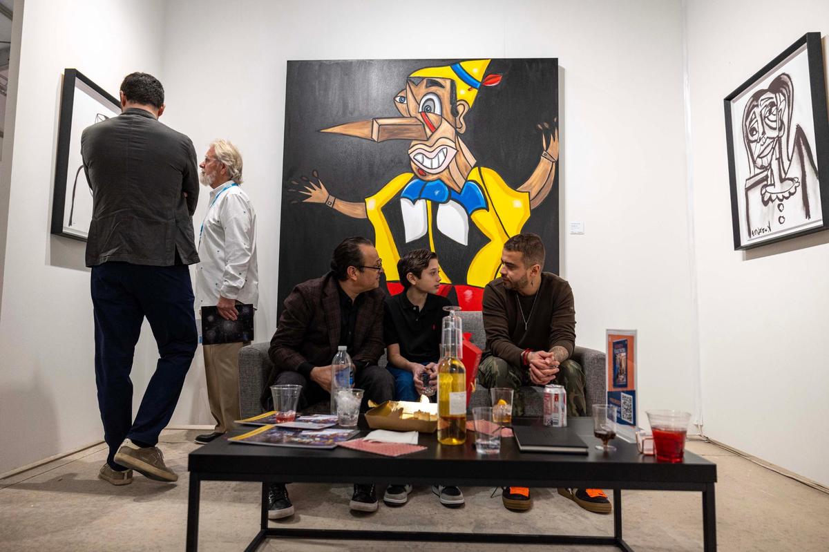 From left to right, Andres Saavedra, Andres Valencia and Guadalupe Valencia sit in front of the ‘Pinocchio’ painting during Art Miami at One Herald Plaza on Tuesday, Dec. 3, 2024, in Miami, Fla. Andres Valencia, 13, painted the art piece.