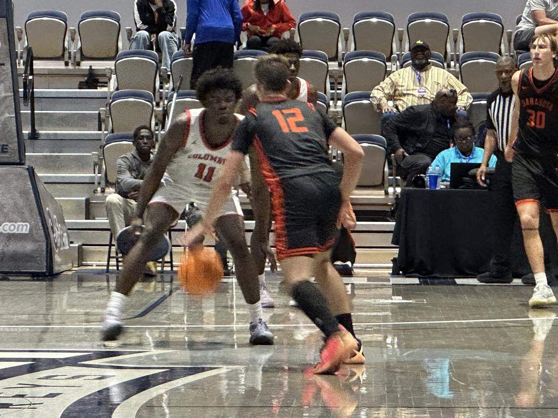 Columbus’ Caleb Gaskins (white jersey) defends Sarasota guard Johnny Lackaff (black jersey) during Saturday’s Class 7A state boys’ basketball championship game at UNF Arena in Jacksonville, Fla.