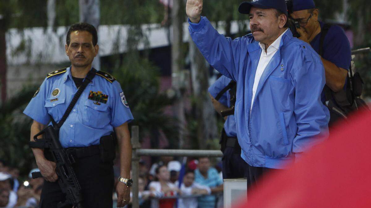 FIle photo of Nicaraguan President Daniel Ortega, right, escorted by one of his armed security guards, waving to a crowd of party faithful during a march for peace, in Managua, Nicaragua, Saturday, July 7, 2018.