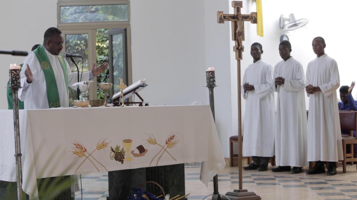 A deacon reads from the Scriptures as altar boys stand by during a Sunday service at the newly built St. Louis Roi de France in Turgeau, Haiti. Still in need of painting, the structure is functional, its priest said.