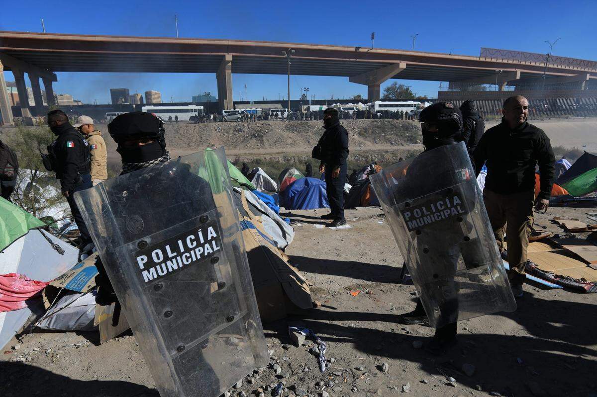 Policías antidisturbios de Juárez, Mexico, ayudan a las autoridades a desalojar a cientos de migrantes del campamento “Pequeña Venezuela” junto al río Bravo. La frontera con Estados Unidos en El Paso es visible al otro lado del río.