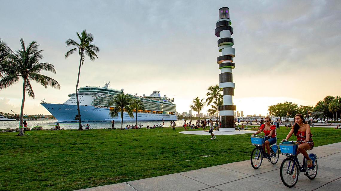 Two people bike down the sidewalk as Royal Caribbean International’s Freedom of the Seas cruise ship sets off down Government Cut past South Pointe Park for a simulated voyage leaving from PortMiami in Miami, Florida, on Sunday, June 20, 2021.