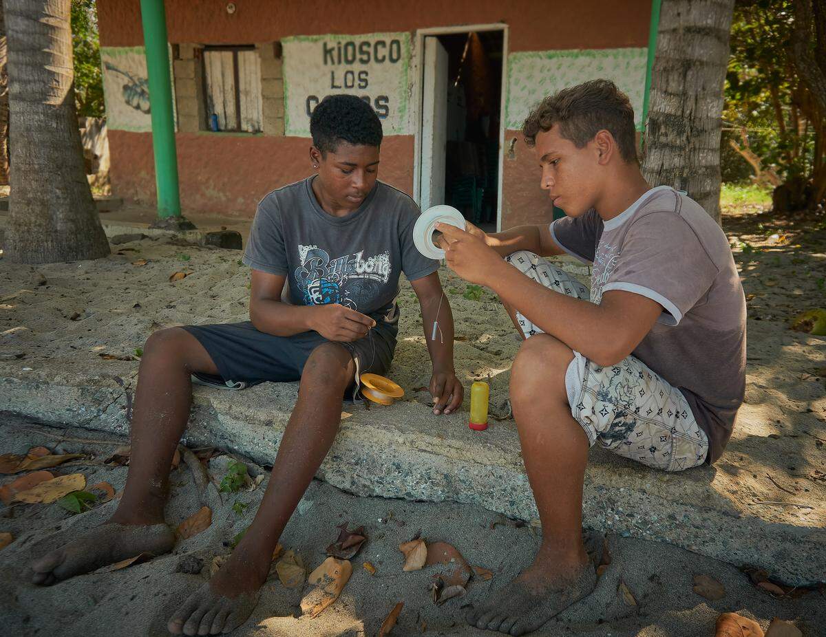 Alexander Ramirez, 17, left, and Javier Gonzalez, 18, prepare their makeshift fishing rods — nylon lines wrapped around plastic disks.