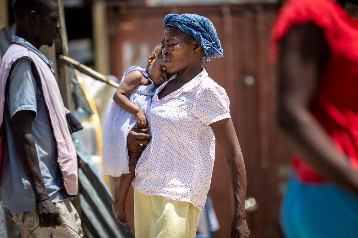 A woman carries a child across the schoolyard at Ecole National Joseph C. Bernard DeFreres displacement camp in Port-au-Prince, Haiti. Gangs have forced more than a million Haitians to flee their homes. Many are living in camps where they are vulnerable to sexual assaults.