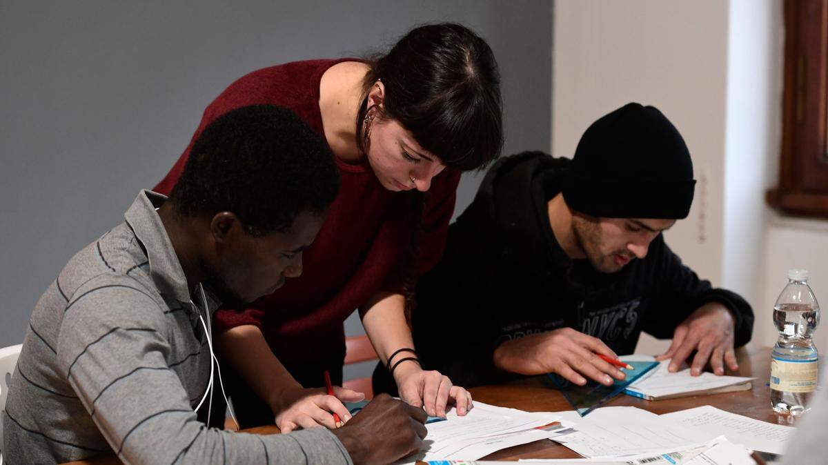 A volunteer help migrants to study in a classroom at the “Lai-Momo” headquarters, a vocational training programme to teach skills in leather bag making to migrants, on November 28, 2017 in Lama di Reno, southern Bologna.