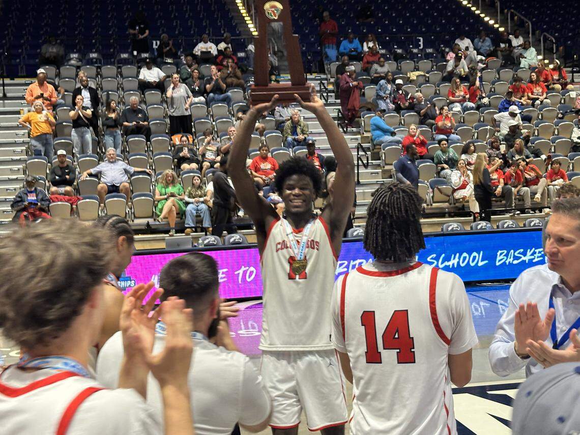 Columbus’ Caleb Gaskins (14) holds the Class 7A boys’ basketball state championship trophy high above his head after the Explorers won it on Saturday at UNF Arena in Jacksonville, Fla.