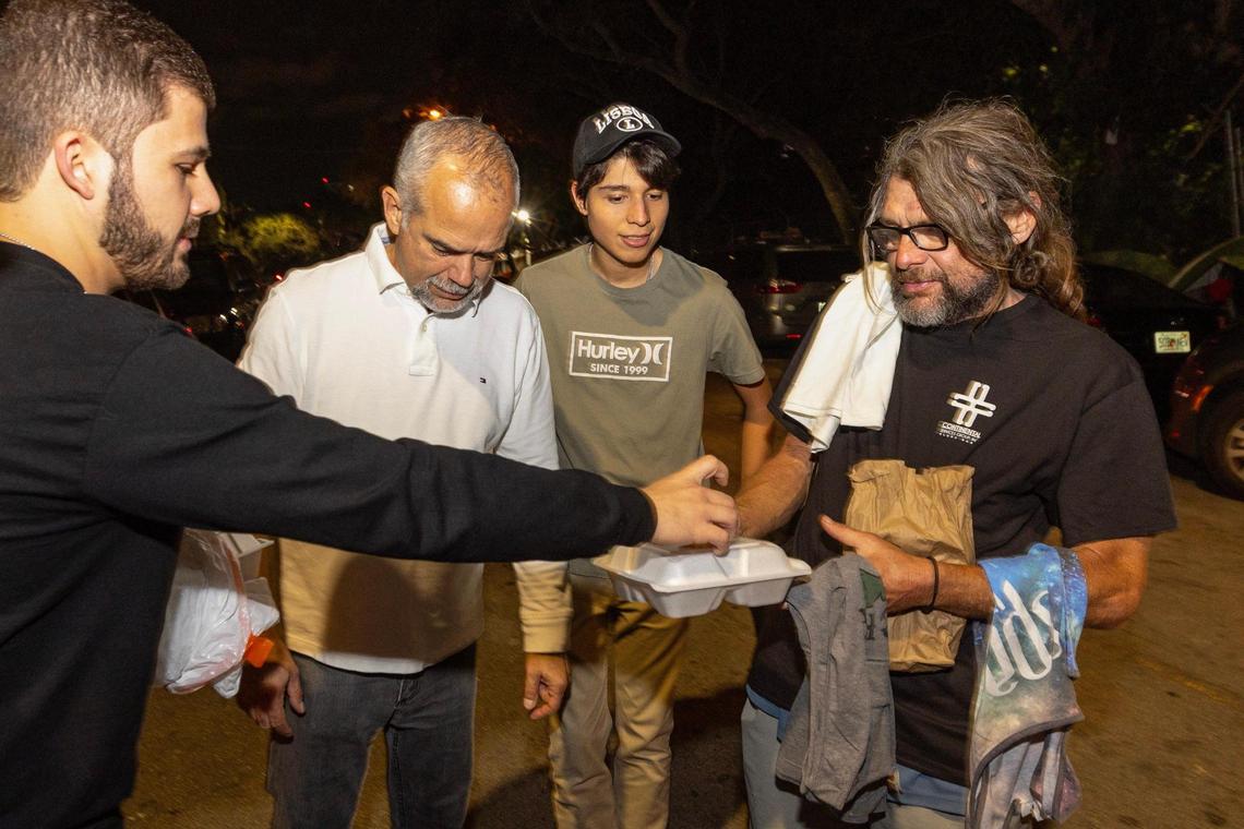 Hermanos de la Calle volunteer Andres Papa hands an unsheltered man a meal during a food distribution event on NW 17th Street in Miami, Florida, on Friday, December 22, 2023.