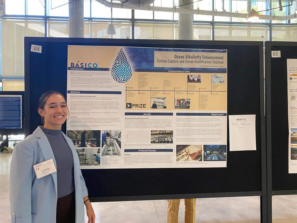Laura Stieghorst stands next to a poster displaying information about her startup, Básico.