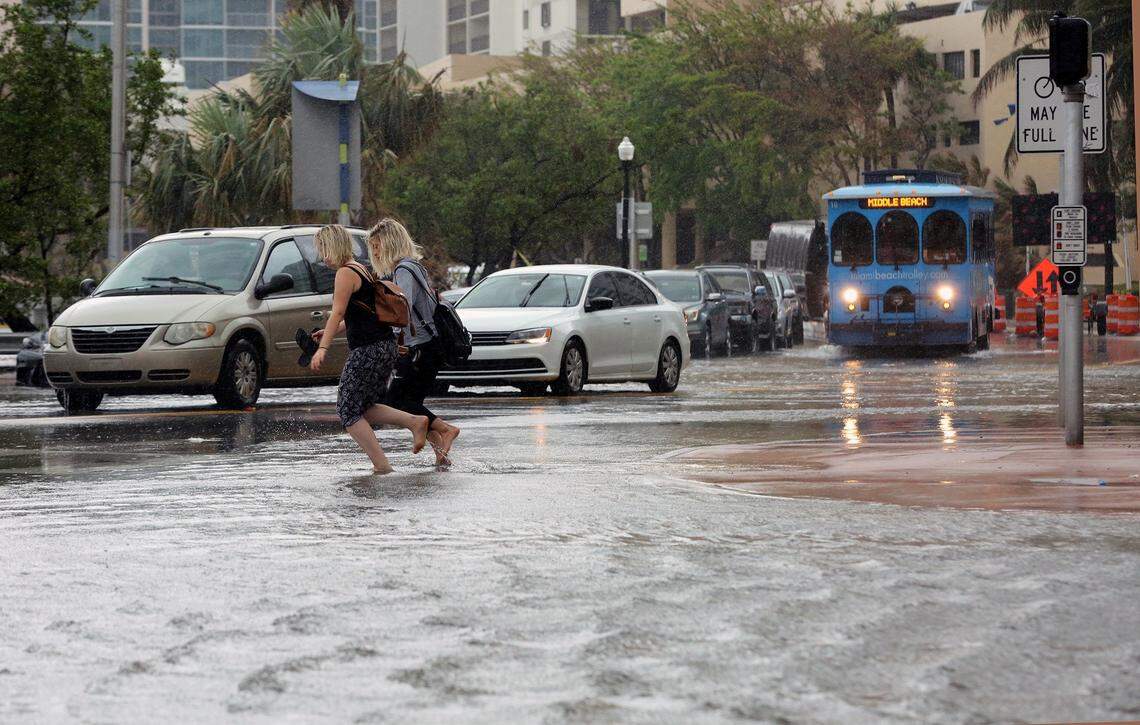 Pedestrians hold their shoes as they run through the flooded streets of Miami Beach on Collins Avenue and 25th street on Thursday, October 5, 2017. Opponents of the proposed convention center hotel argue that it would increase flooding, but the hotel would include water absorption components.