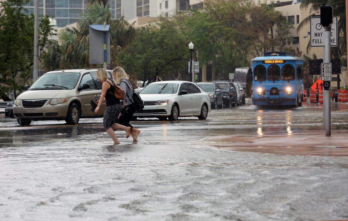 Pedestrians hold their shoes as they run through the flooded streets of Miami Beach on Collins Avenue and 25th street on Thursday, October 5, 2017. Opponents of the proposed convention center hotel argue that it would increase flooding, but the hotel would include water absorption components.