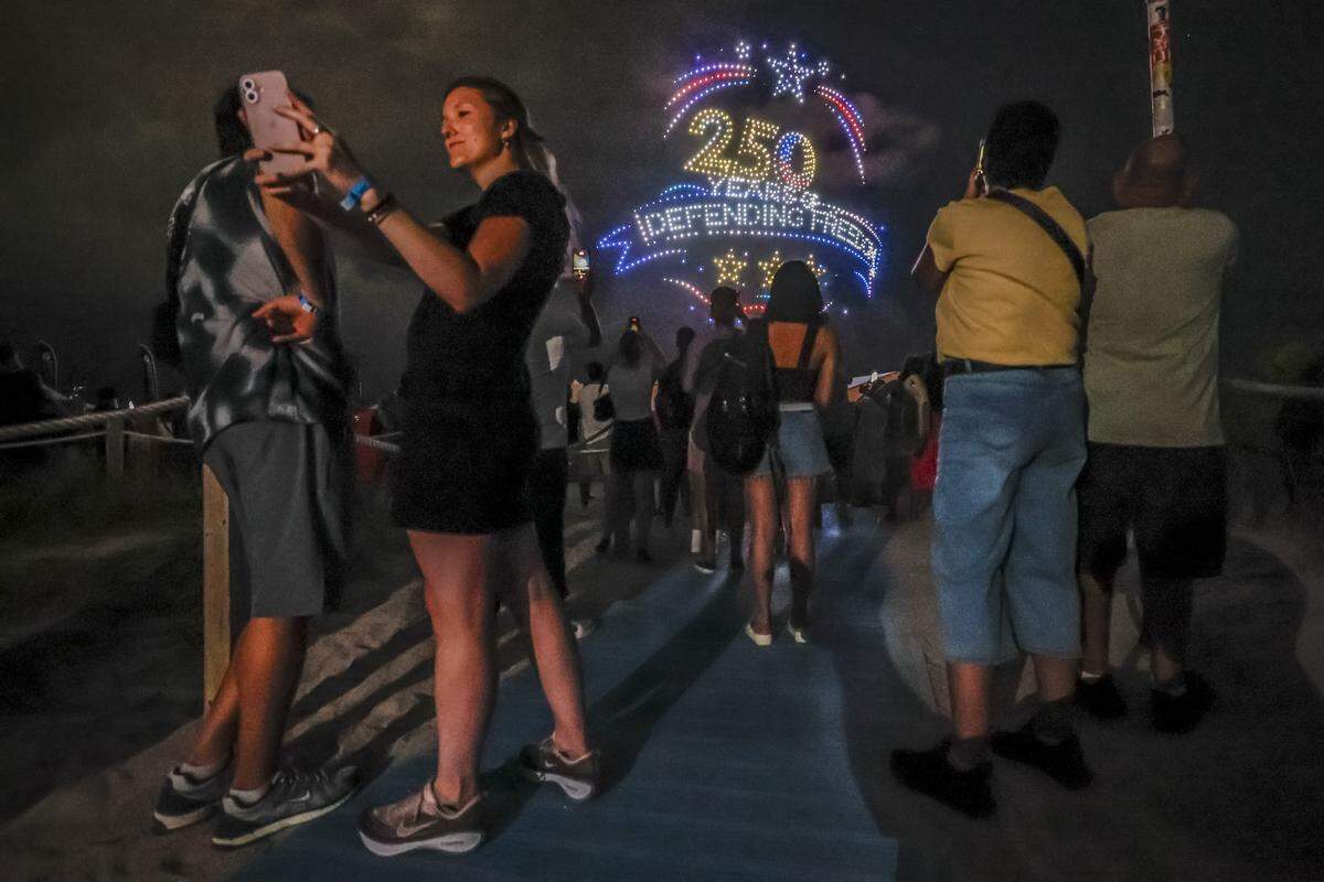 Camila Santiago takes a selfie during a drone show display over the beach behind her during Memorial Day Weekend at the Hyundai Air & Sea Show in Miami Beach, Florida, on Saturday, May 23, 2026.