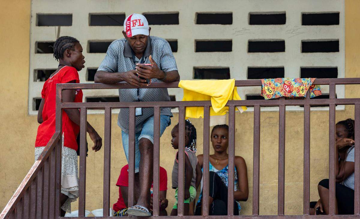 A man passes the time on his cell phone as others sit around and wait at Ecole National Joseph C Bernard DeFreres displacement camp in Port-au-Prince, Haiti, Aug. 27, 2024.
