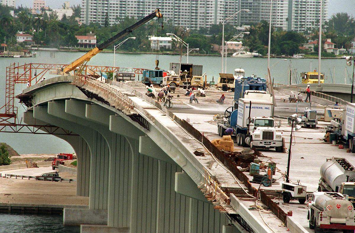 Workers hose down fresh concrete on the MacArthur Causeway that crosses from Miami to Miami Beach .