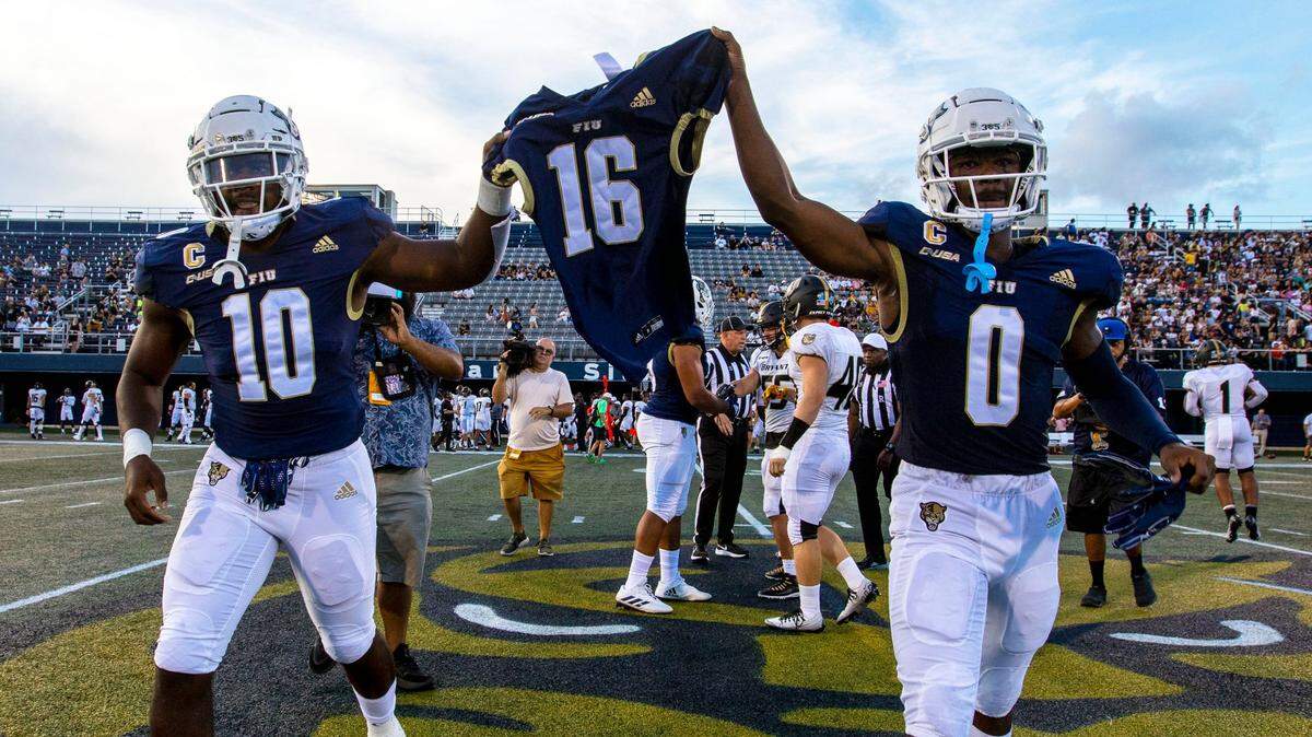 Florida International University captains Donovan Manuel (10) and Tyrese Chambers (0) hold up Luke Knox’s jersey during the coin toss before the first quarter of an NCAA Conference USA football game against Bryant University at Riccardo Silva Stadium in Miami, Florida, on Thursday, September 1, 2022.