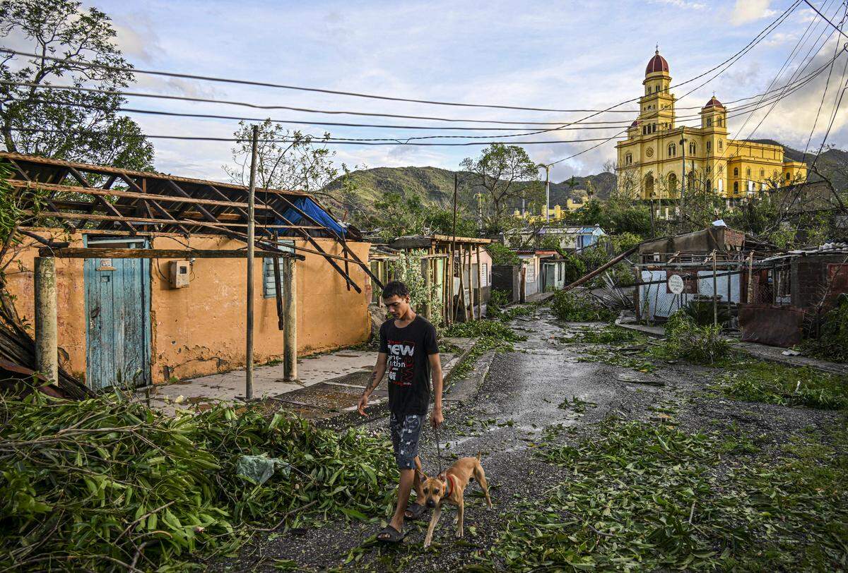 A resident of El Cobre, in the province of Santiago de Cuba, walks his dog past downed trees, power lines and destroyed houses following the passage of Hurricane Melissa, on October 29, 2025.        
