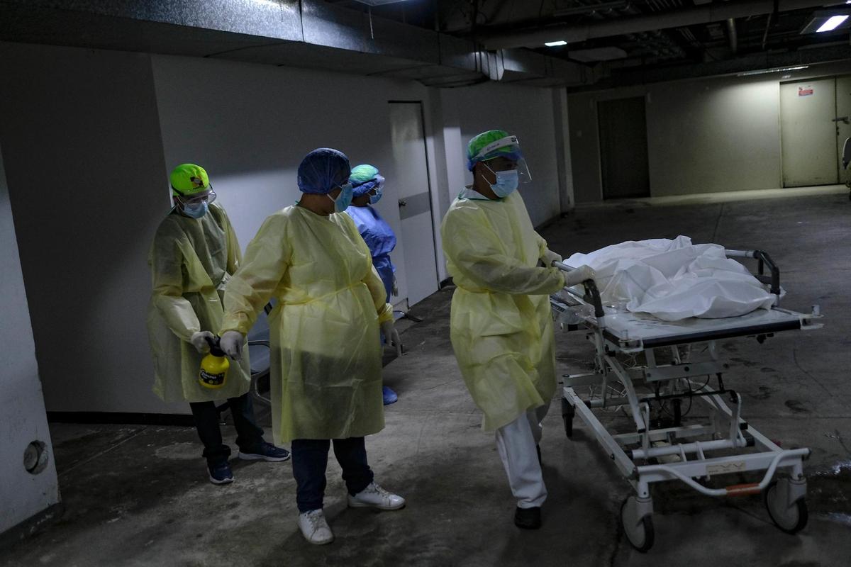 Jessi Duran, center, decked out in protective gear, watches as a health worker pushes a gurney with the body of her aunt, who died from COVID-19, to the morgue at the Ana Francisca Pérez de León II public Hospital in Caracas, Venezuela, on March 23, 2021.
