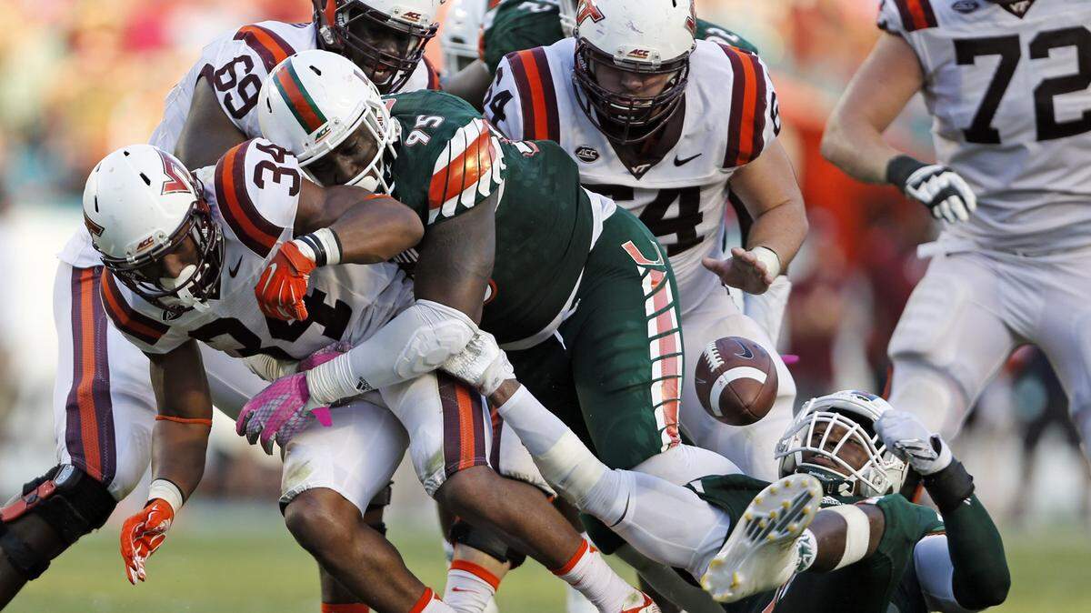 Miami Hurricanes defensive lineman Al-Quadin Muhammad (8) rips the ball from the Virginia Tech Hokies running back Travon McMillian (34) as Miami Hurricanes defensive lineman Anthony Moten (95) tackles McMillian on Oct. 17, 2015.