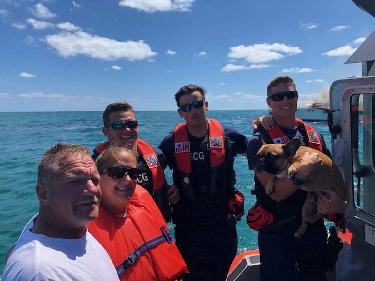 A man, a woman and their dog stand on the deck of a U.S. Coast Guard boat with the men who rescued them in the water after their boat caught fire off Islamorada Wednesday, April 17, 2019. US Coast Guard Station Islamorada photo