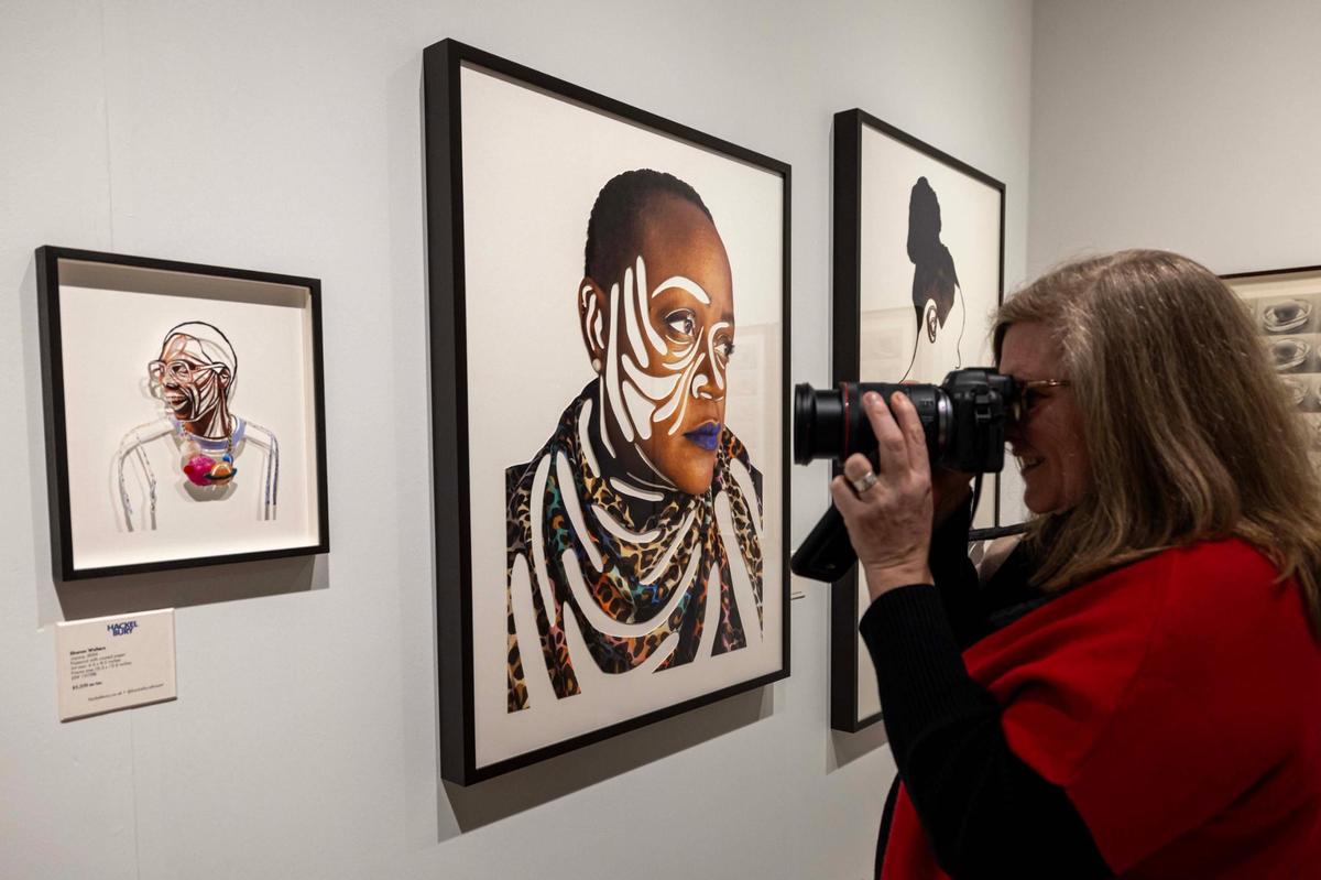 A guest takes photos of art created by London-based portrait artist Sharon Walters during Art Miami at One Herald Plaza on Tuesday, Dec. 3, 2024, in Miami, Fla.