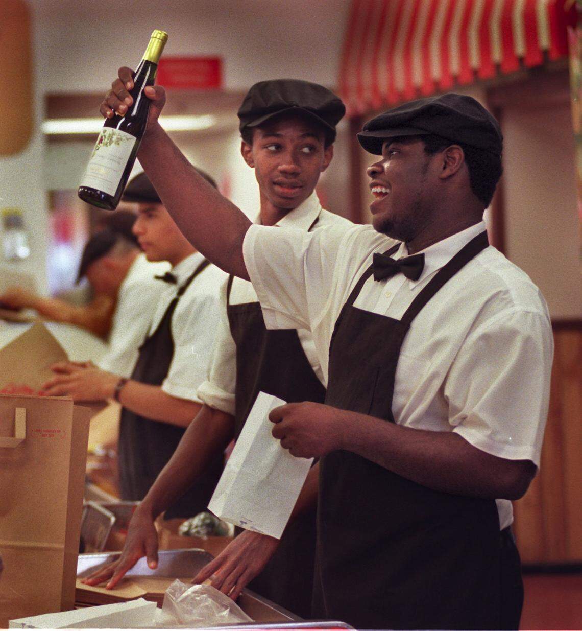 Epicure worker Billy Belony, right, teases a customer at check-out as he bags up several bottles of champagne and wine. Worker Charley Etienne is at left..