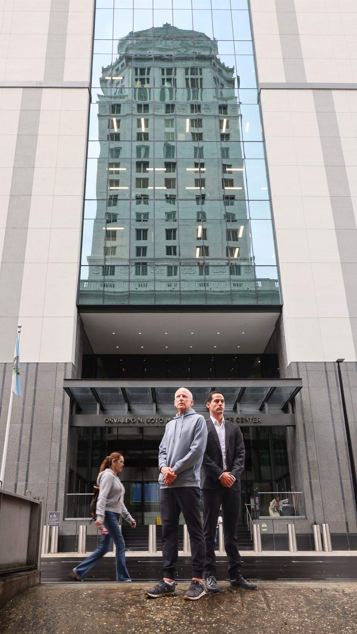 Pablo Langesfeld, left, who lost his daughter and son-in-law in the 2021 Champlain Towers collapse, stands with his son Martin, right, outside the Osvaldo N. Soto Miami-Dade Justice Center in Miami, Tuesday, April 7, 2026. Langesfeld, now battling advanced pancreatic cancer, is suing Oscar Health Insurance for denying coverage of a drug therapy his doctors recommend, underscoring broader struggles over access to treatment.