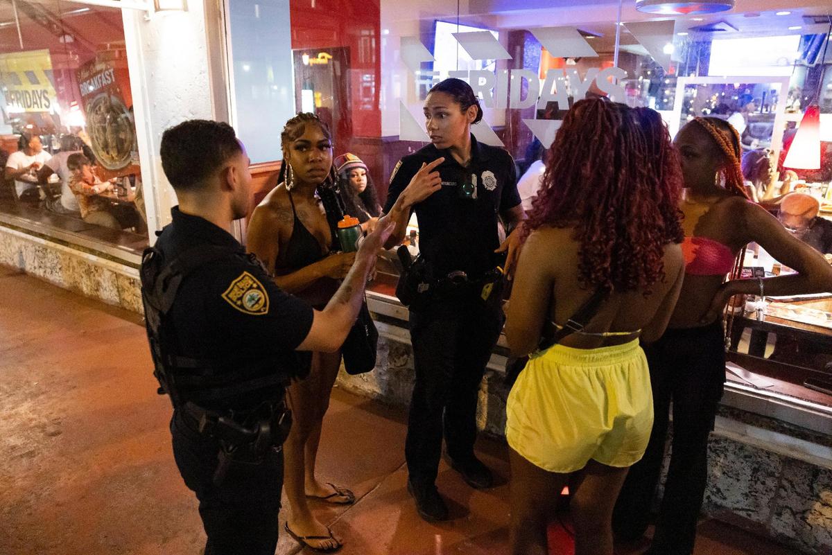 Miami Beach police officers talk to a group of women who were dancing near TGI Fridays off Ocean Drive during spring break on Friday, March 15, 2024, in Miami Beach.&nbsp;